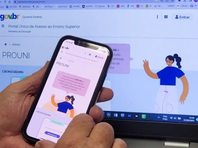 Pessoa acessando o site do Prouni pelo celular, com o portal do Prouni no fundo, em um computador