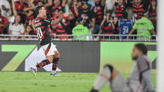 Arrascaeta, do Flamengo, comemora gol enquanto Lucas Arcanjo, do Vitória, lamenta sentado no gramado