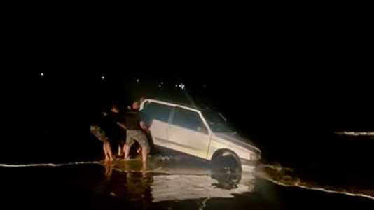 Veículo prata atolado na areia sendo resgato por policiais