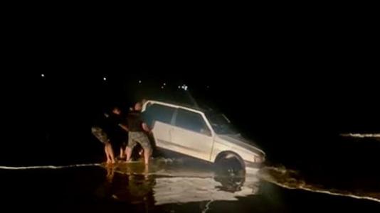 Veículo prata atolado na areia sendo resgato por policiais