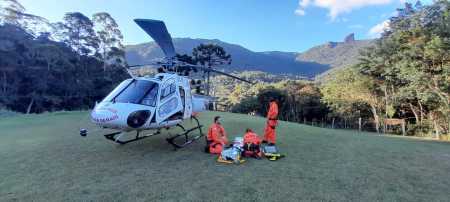 Três bombeiros atendem vítima, que está deitada em uma prancha e coberta com manta térmica, ao lado de um helicóptero