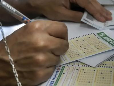 Pessoa marcando número em volantes da Mega-Sena com caneta