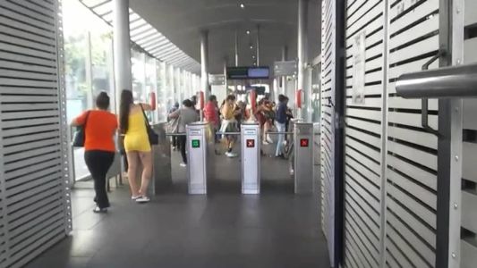 A mulher de amarelo passa o cartão de vale-transporte para a senhroa de laranja, após receber uma quantia em dinheiro