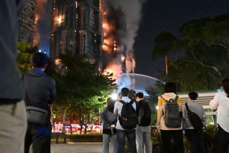 Testemunhas observam a densa fumaça e as chamas que se elevam durante um grande incêndio no conjunto residencial Wang Fuk Court, no distrito de Tai Po, em Hong Kong, em 26 de novembro de 2025
