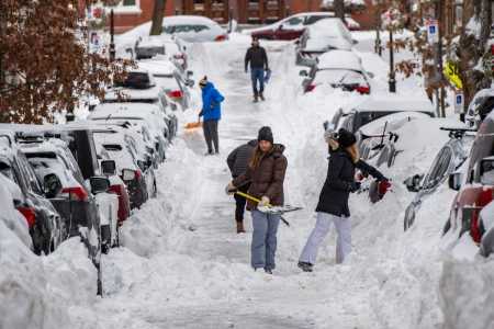 Pessoas removem a neve com pás ao longo de uma rua residencial no bairro de Charlestown, em Boston, Massachusetts, em 26 de janeiro de 2026.
