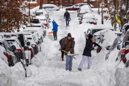 Pessoas removem a neve com pás ao longo de uma rua residencial no bairro de Charlestown, em Boston, Massachusetts, em 26 de janeiro de 2026.