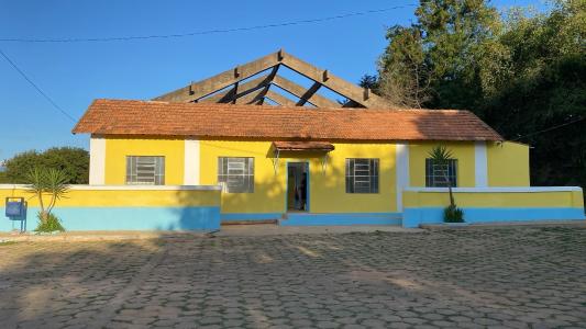 Imagem mostra casa grande, pintada de amarelo, azul e branco com árvores verdes ao fundo