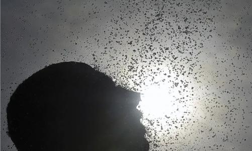 Silhueta de um homem contra o sol e vários pingos d'água espalhados pela imagem