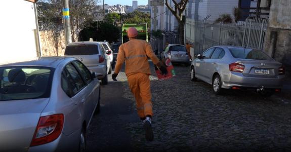 Foto mostra gari correndo atrás de caminhão de lixo em rua de BH