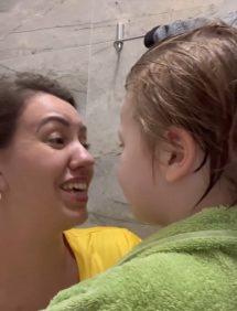 Mãe, de amarelo, se emociona com filho, envolto em toalha verde