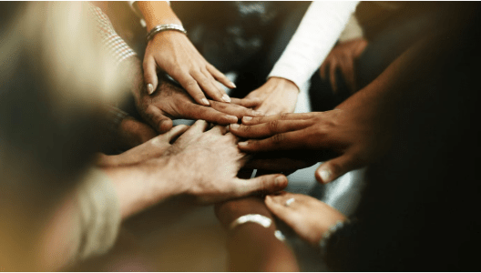 mãos sobrepostas de pessoas de diversas raças simbolizando união e cooperação