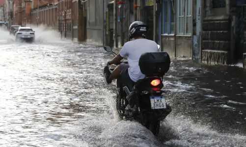 Foto mostra motociclista passando por rua alagada no Rio de Janeiro