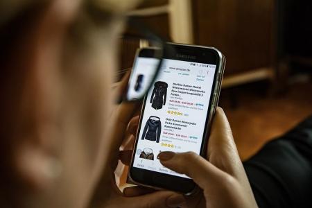 Uma pessoa branca, com unhas pintadas de cor bege, olha casacos de frio no site da Amazon pelo telefone celular.