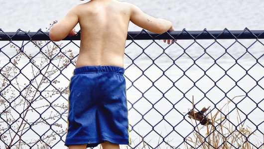 Foto mostra menino sem camisa debruçado em grade