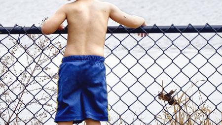Foto mostra menino sem camisa debruçado em grade