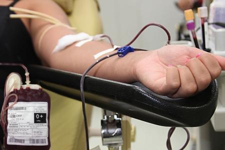 Pessoa doando sangue. Na imagem, é possível ver um braço de uma mulher com as unhas feitas. Há um dispositivo de retirada de sangue para doação em seu braço e uma bolsa de sangue O positivo próximo