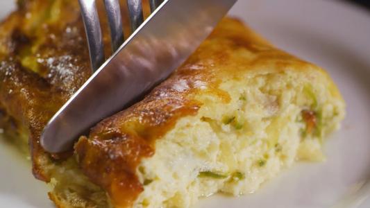 Utilizando um garfo e uma faca, uma pessoa corta um pedaço de gratin de bacon com queijo