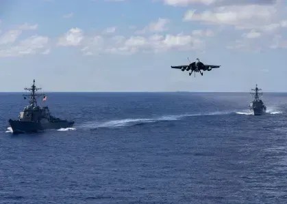 Destróieres de mísseis guiados da classe Arleigh Burke, USS Mahan, à esquerda, e USS Bainbridge, navegam em formação enquanto um FA-18 Super Hornet, a bordo do USS Gerald R. Ford (CVN 78), inicia pouso