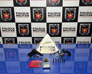 Foto mostra pistolas e cartuchos de munição em uma mesa azul com o monograma da polícia militar ao fundo