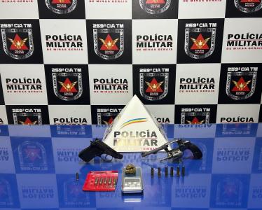 Foto mostra pistolas e cartuchos de munição em uma mesa azul com o monograma da polícia militar ao fundo