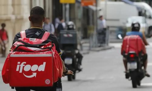 Motoqueiros com baús do iFood pilotam veículos por ruas de cidade do Brasil