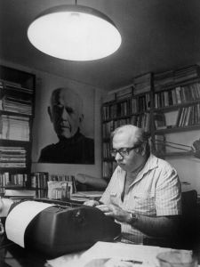 Luis Fernando Verissimo escrevendo na máquina de datilografar; ao fundo, a foto do pai, Erico Verissimo