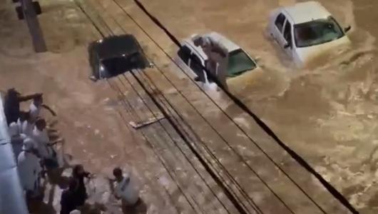 Foto mostra rua alagada, carros e pessoas tentando se salvar