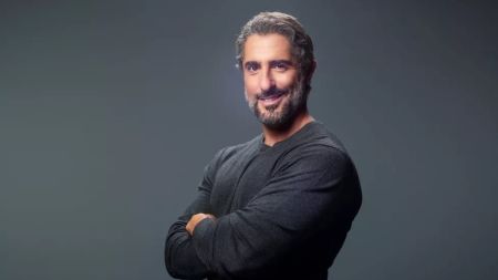 Marcos Mion de braços cruzados, camisa preta, sorrindo para foro