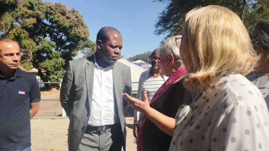 Ministro Almeida. Ele é um homem preto, careca, e na imagem conversa com duas mulheres com as mãos para trás. Almeida usa terno cinza e blusa social branca.