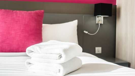 Foto mostra toalhas brancas, travesseiro vermelho e quarto de motel