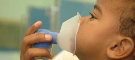 Um garoto usa um nebulizador, com a máscara cobrindo seu nariz e boca