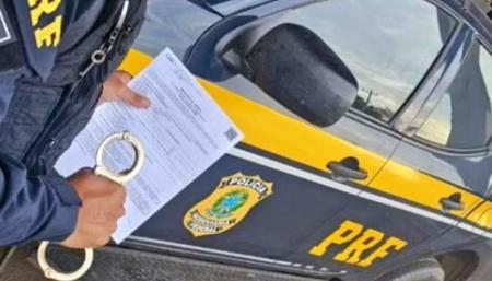 Foto mostra viatura da Polícia Rodoviária Federal e mandado de prisão
