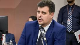 Homem branco com cabelo e barba de cor castanho escuro com terno azul marinho.