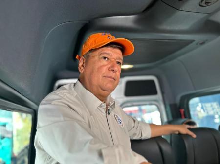 Carlos Viana é um homem branco, de camisa social branca e boné laranja. Ele está em pé em uma van.