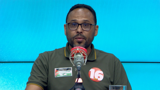 Wanderson Rocha é um homem preto, usa óculos de grau, camisa verde musgo com adesivos com a bandeira da Palestina e com o número 16.