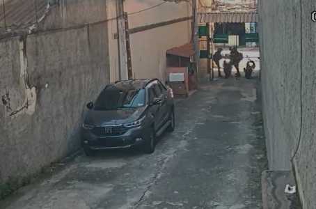 imagem de câmera de segurança mostra um beco com carro estacionado e duas pessoas cometendo assalto a um motociclista