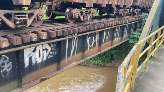 Na foto é possível ver a linha do trem em uma ponte e por baixo o rio