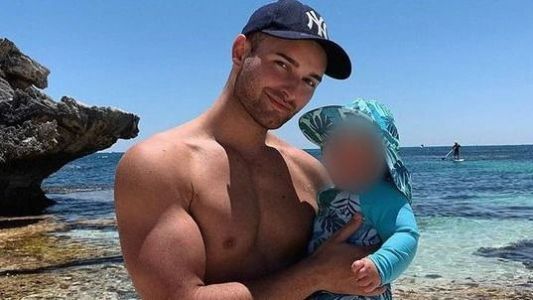 Homem sem camisa de boné segurando um bebê em uma praia