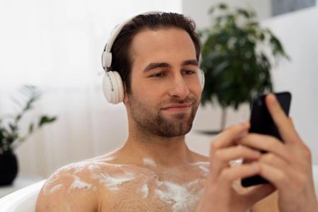 Um homem tomando banho, usando fones de ouvido e segurando um celular