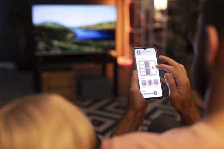 Homem segurando um celular em frente à TV