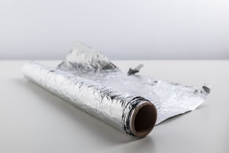 Rolo de papel alumínio em cima de uma superfície branca, com fundo cinza