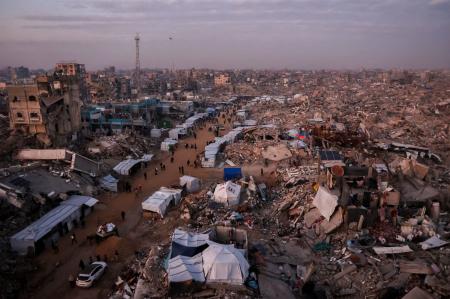 Palestinos caminham por entre tendas que se alinham nas ruas em meio aos escombros de edifícios destruídos em Jabalia, no norte da Faixa de Gaza, em 18 de fevereiro de 2025, enquanto as pessoas retornam às partes do norte de Gaza