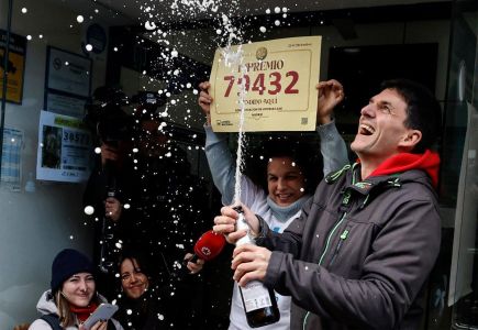 Vendedores de loteria posam para fotos em frente à sua loja, segurando um bilhete premiado com o primeiro prêmio da loteria de Natal espanhola "El Gordo" (O Gordo), em Madri