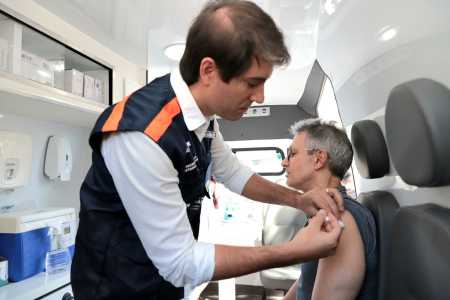 Fábio Baccheretti, secretário de Saúde de Minas, aplica dose da vacina contra a gripe em um dos braços do governador Romeu Zema, dentro de uma ambulância.