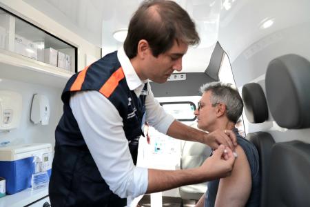 Fábio Baccheretti, secretário de Saúde de Minas, aplica dose da vacina contra a gripe em um dos braços do governador Romeu Zema, dentro de uma ambulância.