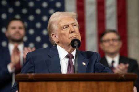 Donald Trump em um palanque, com microfone, na frente de uma bandeira dos EUA