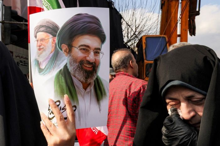 Uma mulher segura um cartaz do novo líder supremo do Irã, o aiatolá Mojtaba Khamenei (à direita), ao lado de seu falecido pai, Ali Khamenei, durante uma manifestação em apoio a ele na Praça Enghelab, em Teerã, em 9 de março de 2026
