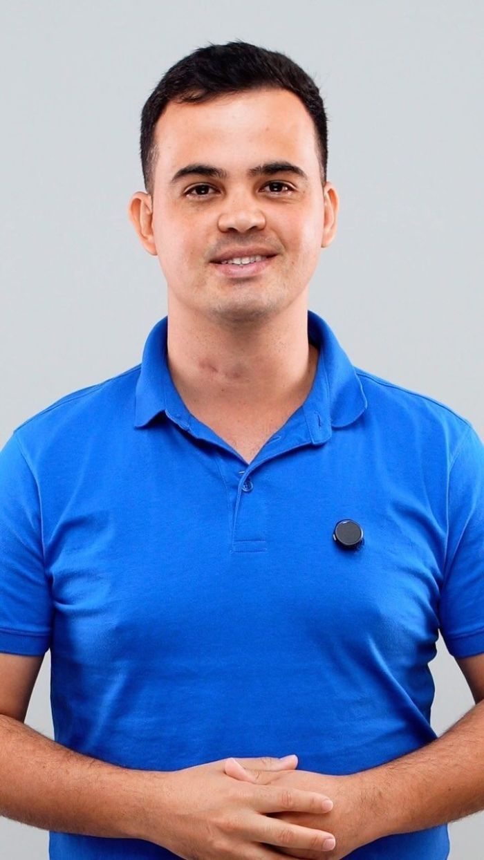 Cabo Junio é um homem branco, de cabelos pretos curtos. Na imagem ele está com as mãos cruzadas e usa uma camisa azul.