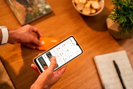 Pessoa utilizando o aplicativo do Inter pelo celular com uma mão e o cartão da instituição financeira na outra.