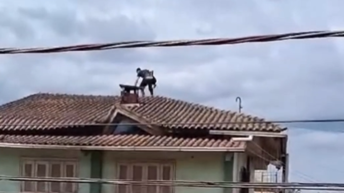 Jovem em cima do telhado de casa de três andares, após temporais no Rio Grande do Sul, resgatando cadela